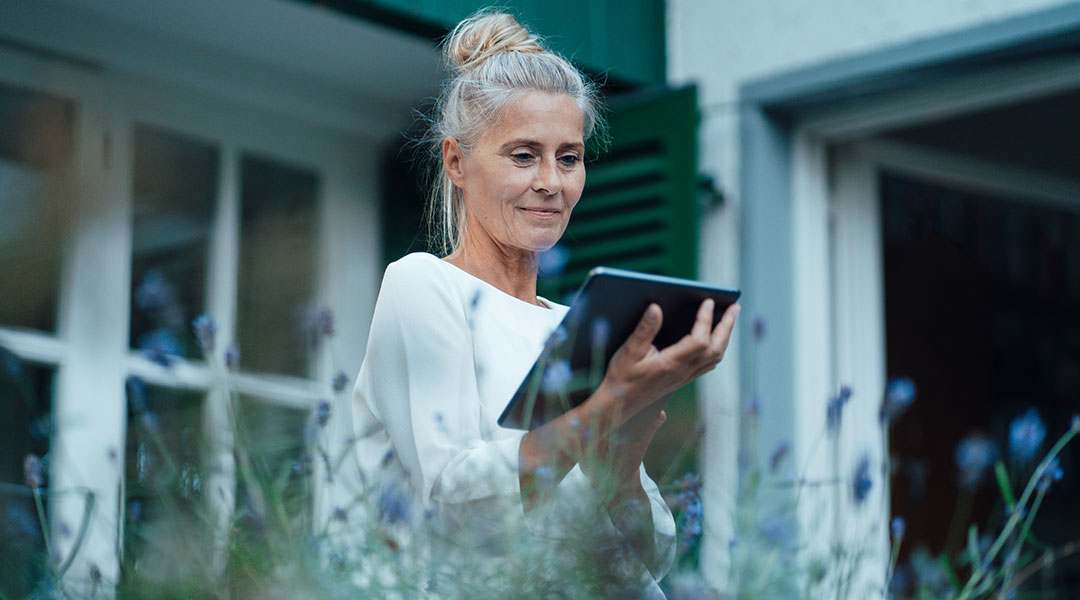 an older lady with a high bun in her garden looking down at her ipad